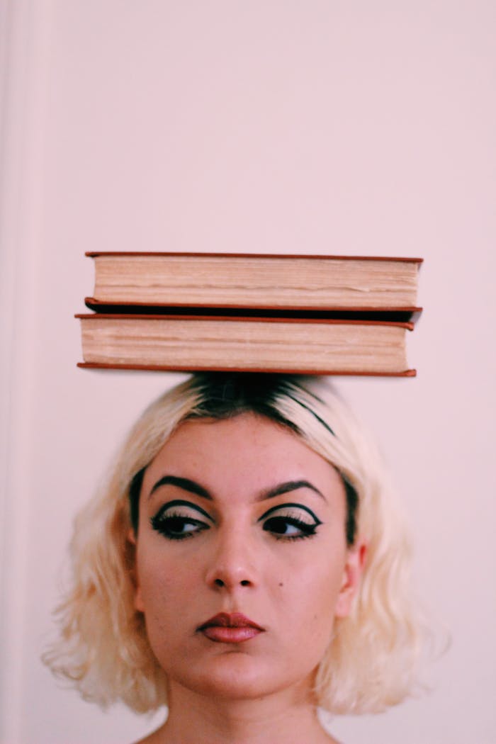 Close-up of a woman balancing books on her head with a serious expression.